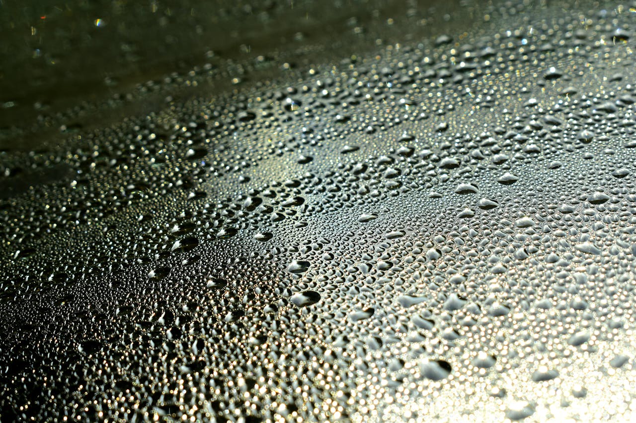 Macro shot of dew droplets forming intricate patterns on a surface, highlighting texture and liquidity.