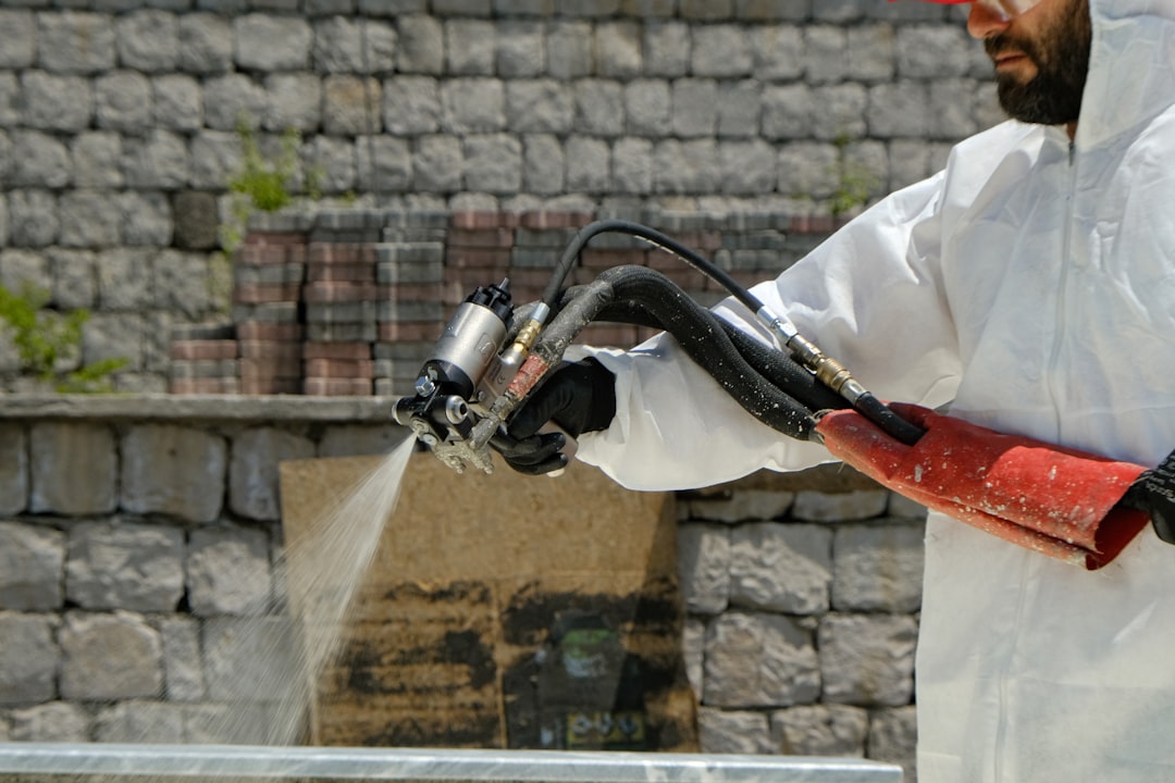 a-man-in-a-white-coverall-spraying-water-with-a-hose-nwnqeydv8ba